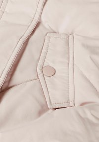 Light pink puffer jacket fabric with a visible snap button and quilted texture. Features a flap pocket at the front below the button.