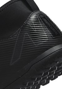 Zapato de fútbol negro con parte superior sintética texturizada, detalles acanalados y suela de goma con un patrón de agarre con tacos.