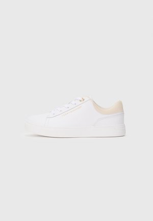 Weiße Low-Top-Sneaker mit beigefarbenem Kragen, weißen Schnürsenkeln und goldenem "Tommy Hilfiger"-Logo an der Seite, seitlich auf grauem Hintergrund dargestellt.