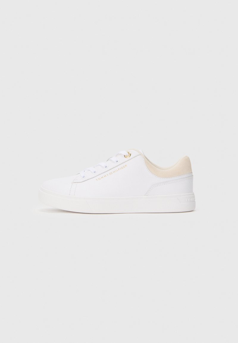 Hvite lavsko med beige krage, hvite snørebånd og gull "Tommy Hilfiger" logo på siden, vist i profil mot grå bakgrunn.