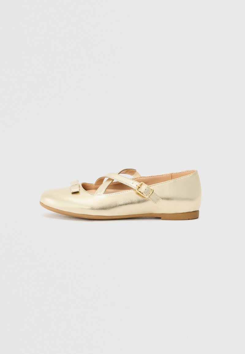 Chaussure plate Mary Jane dorée brillante avec une bride à boucle et un petit détail nœud sur un fond clair uni.