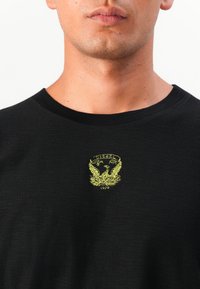 T-shirt noir en tissu doux, avec un logo brodé jaune représentant un phénix et le mot "DIESEL" au-dessus de l'année "1978".