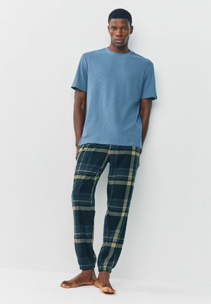 Blue short-sleeved ribbed t-shirt paired with green and navy plaid pants featuring elastic cuffs. Soft, casual fabric with a relaxed fit.