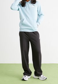 Vaaleansininen huppari kengurun taskulla ja logolla; yhdistettynä mustiin collegehousuihin. Kengät ovat valkoiset mustilla yksityiskohdilla. Vihreä lattia.