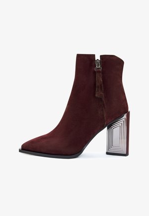 Bottine en daim bordeaux, hauteur de cheville, avec un bout pointu, une fermeture éclair sur le côté et un talon bloc réfléchissant aux motifs géométriques.