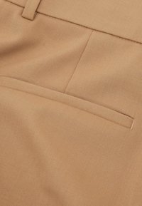 Prim-plan cu material bej ce prezintă un buzunar orizontal cu tăietură aplicată și detaliu cusut pe o piesă vestimentară croită.