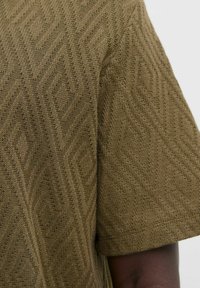 Olivgrön, stickad tyg med en strukturerad diamantmönster. Korta ärmar och en avslappnad passform. Synligt sömnadsdetalj över hela plagget.