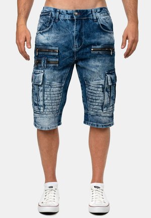 Herren blaue Denim-Cargoshorts mit mehreren Reißverschluss- und Klappentaschen, getragen mit weißen Sneakers.