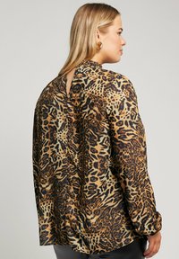 Blusa con stampa leopardata, maniche lunghe, scollatura media e dettaglio a chiave sulla schiena. Tessuto setoso con una miscela di colori marrone, nero e beige.