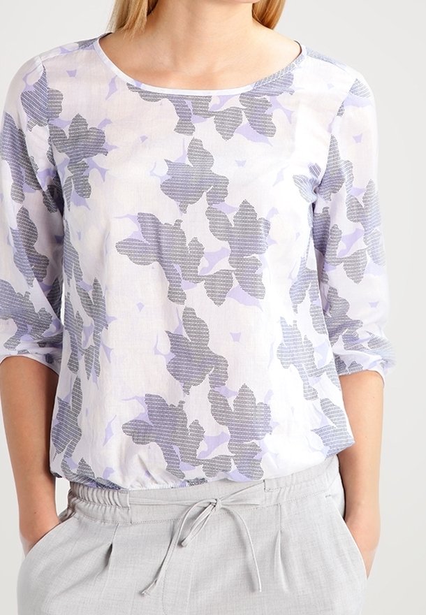 Blouse transparente à manches longues avec un motif floral en lavande et gris sur un fond clair. Encolure arrondie et coupe décontractée.