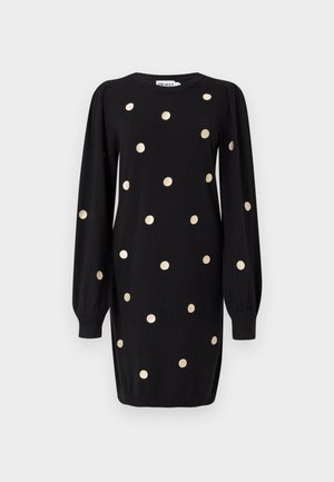 Černé šaty s dlouhými rukávy, zlatými puntíky, pletenými manžetami a kulatým výstřihem, vystavené na jednoduchém světle šedém pozadí.