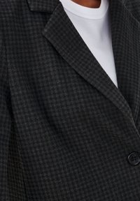 Blazer grigio scuro a motivo con una texture houndstooth, dotato di revers a picco, chiusura a un pulsante e una morbida fodera interna bianca.