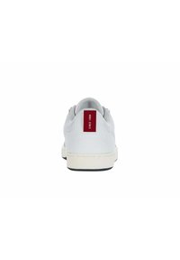 Fehér sneaker texturált szövet felsőrésszel, gumi talppal és piros díszítéssel a saroknál, dombornyomott logóval és minimalista dizájnnal.