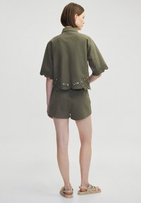 Chemise vert olive à manches courtes avec un ourlet festonné et des clous décoratifs, associée à un short assorti. Texture lisse et coupe décontractée.