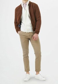Bruine suède bomberjack over een witte kabelgebreide cardigan, beige chino's en witte sneakers. De outfit heeft een textuur en een casual stijl.