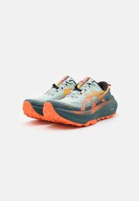 Baskets de trail de couleur bleu clair avec des accents orange et noir, tige texturée, lacets noirs, semelle rembourrée et semelle extérieure robuste pour une meilleure adhérence.