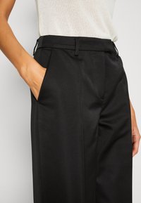 Black tailored trousers with a smooth texture, featuring a straight leg, side pockets, and a belt looped waistband.