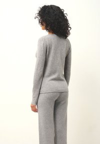 Grauer Strickpullover mit langen Ärmeln und rundem Ausschnitt, kombiniert mit passenden weit geschnittenen Hosen. Weiche Textur, lässiges Design und nahtlose Verarbeitung.