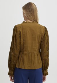 Blusa peplum marrone con maniche lunghe ricamate. Presenta un colletto arricciato e intricati motivi intagliati sulle maniche.