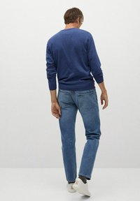 Suéter de punto azul con mangas largas, combinado con jeans de denim azul claro. El modelo lleva zapatillas blancas. Ajuste simple y casual visto desde atrás.