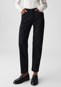 Pantaloni neri tagliati a cropped con una vestibilità dritta, tasche frontali e chiusura a bottone. Tessuto di cotone liscio, abbinati a mocassini neri.