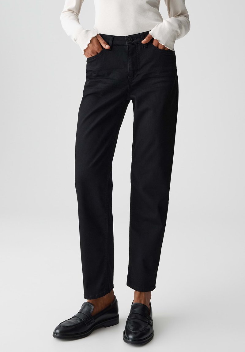 Pantaloni neri tagliati a cropped con una vestibilità dritta, tasche frontali e chiusura a bottone. Tessuto di cotone liscio, abbinati a mocassini neri.