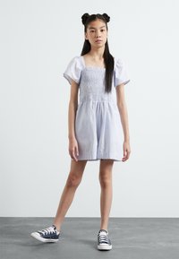 Gestreiftes, blau-weißes Kurzkleid mit gerafftem Oberteil und Puffärmeln, kombiniert mit marineblauen Sneakers. Flach, glatte Textur.