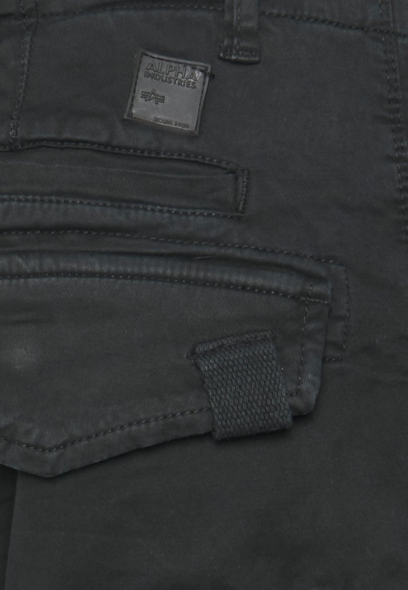 Pantalones cargo negros que presentan múltiples bolsillos, una tela texturizada y una etiqueta de marca de goma, destacando un diseño utilitario.