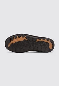 Semelle de chaussure en caoutchouc noir avec une surface texturée, dotée de profondes rainures pour l'adhérence et d'une accentuation marron avec le logo "Fluchos".