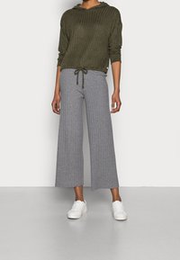 Sweat à capuche côtelé vert olive avec cordon de serrage et manches longues, associé à un pantalon large côtelé gris clair, complété par des baskets blanches.