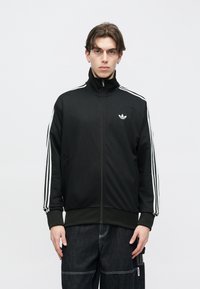 Μαύρο μπλουζάκι με φερμουάρ και υφή, με λευκές τρεις ρίγες και μικρό λευκό λογότυπο στο στήθος.