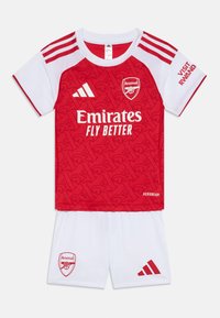 Röd och vit ungdomsfotbollskit; tröjan har en strukturerad röd design med Arsenal-logotyp, vita shorts och tre-rands axeldetaljer.