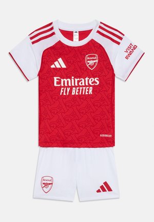Punasilja ja valge noorte jalgpallivarustus; särgil on tekstureeritud punane disain Arsenalile kuuluva logoga, valged lühikesed püksid ja triibuline õlavarreaktsent.