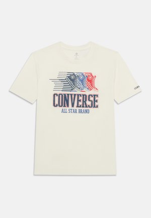 T-shirt blanc présentant trois baskets Converse stylisées en bleu et rouge au-dessus d’un grand texte « CONVERSE ALL STAR BRAND » sur le devant.
