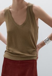 Olivengroene mouwloze top met een V-hals, gemaakt van een gestructureerde stof. Gecombineerd met een roestkleurige suède rok en een zilveren armband.