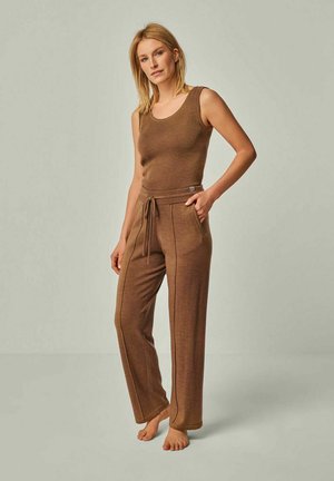 Braun gerippter Tank-Top mit passenden Jogginghosen. Die Hosen verfügen über Seitentaschen und kontrastierende Nähte. Das Modell steht barfuß vor einem neutralen Hintergrund.