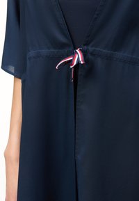 Ρούχο ναυτικού μπλε με κοντά μανίκια, με μπροστινή λεπτομέρεια δέσιμου από κορδέλα με ρίγες σε κόκκινο, άσπρο και μπλε στο στήθος.