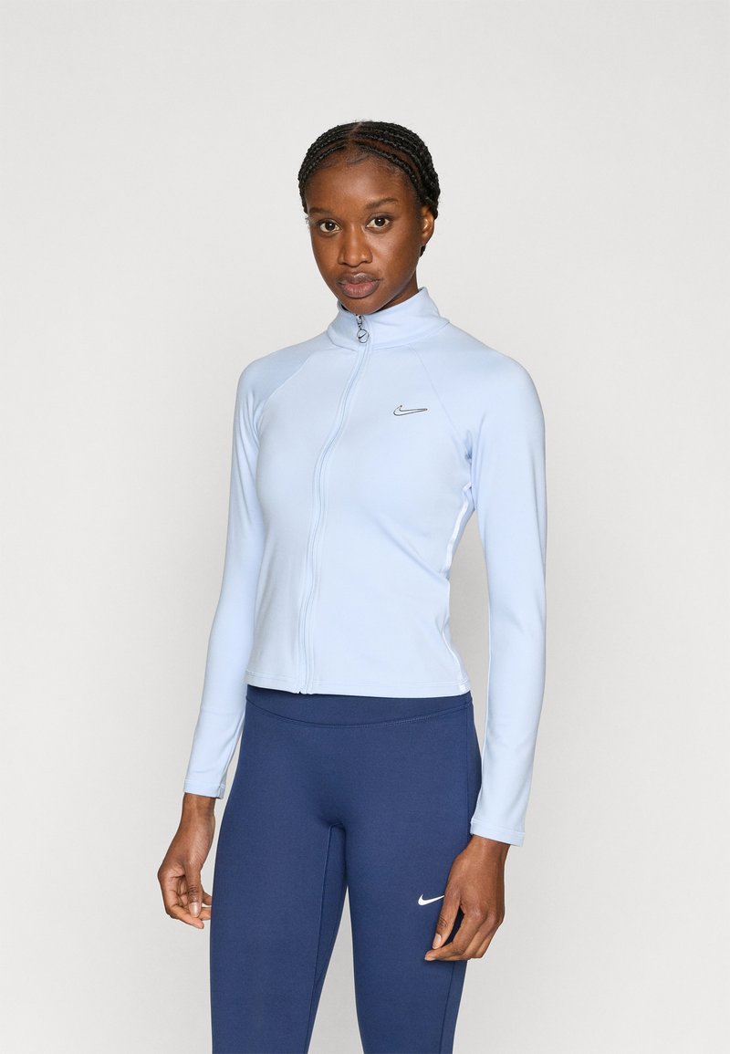 Svetlo modra jopa z zadrgo in visokim ovratnikom, izdelana iz gladkega materiala. Ima dolge rokave in nežen logotip na prsih. Kombinirana s temno modrimi pajkicami.