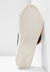 Semelle d'une chaussure blanche à semelle en caoutchouc affichant la taille 37, avec des motifs de bande de roulement croisés et géométriques, positionnée sur un fond d'angle blanc.