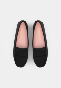 Svarta platta skor med moccasin-design, med en sydd ovandel och en mjuk rosa innersula med gulddetaljer. Slät textur, rund tå.