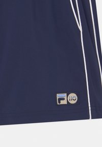 Námornícky modrá látka s bielým lemováním a malou obdélníkovou nášivkou s abstraktními tvary v světle modré a béžové barvě.