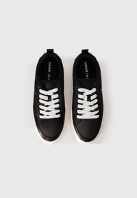Sneakers neri con una superficie liscia, lacci bianchi e suola bianca a contrasto. Logo del marchio visibile sul lato e all'interno.