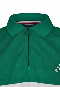 Polo vert avec une courte fermeture éclair, texture tricotée, rayure blanche contrastante et "PARIS" imprimé en blanc sur la poitrine. Étiquette de marque : HECHTER.