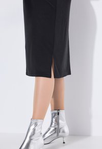 Un vestido negro de longitud a la rodilla con una abertura lateral, combinado con botas metálicas plateadas hasta el tobillo con cierre de cremallera y un tacón tipo kitten.