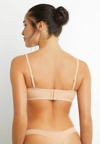 Beige bralette with adjustable straps and a hook closure, featuring a smooth texture and minimalistic design. Thin matching briefs visible.