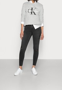 Sudadera gris de Calvin Klein con logo negro, combinada con jeans skinny negros con detalles desgastados y zapatillas blancas. Textura suave.