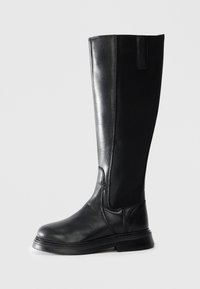 Botte en cuir noire, montant jusqu'au genou, avec panneau latéral élastique et petit talon, vue de l'extérieur sur fond blanc.