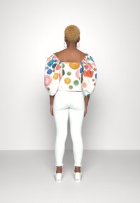 Top blanco sin hombros con lunares coloridos y mangas abullonadas, combinado con jeans ajustados blancos y zapatos blancos.