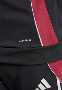 Ropa activa negra con acentos en rojo y blanco. Presenta un tejido texturizado y el logo "AEROREADY", que mejora la transpirabilidad y la comodidad.