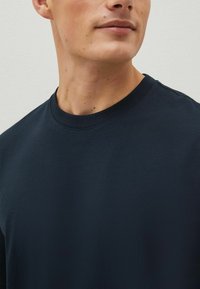 Sötét tengerészkék kerek nyakú póló, puha anyagból készült, rövid ujjakkal és sima textúrával, látható minták vagy díszítések nélkül.